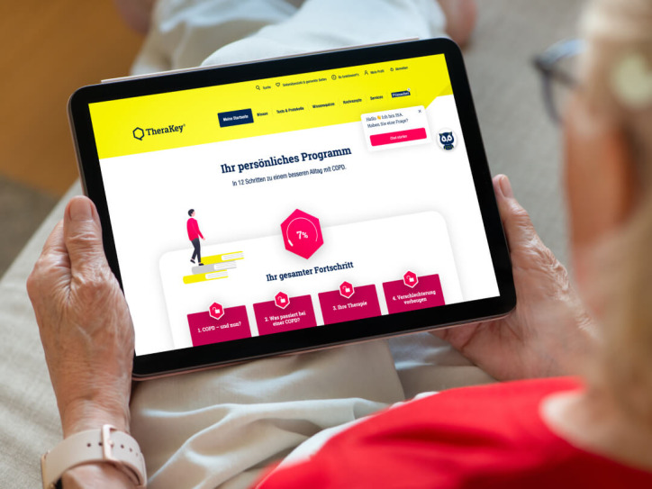 Eine Frau hält ein Tablet und betrachtet die TheraKey-Website auf dem Bildschirm.
